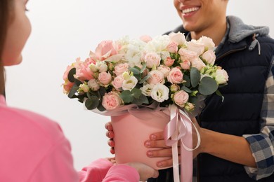 Happy delivery man giving gift box with beautiful floral composition to woman on white background, closeup