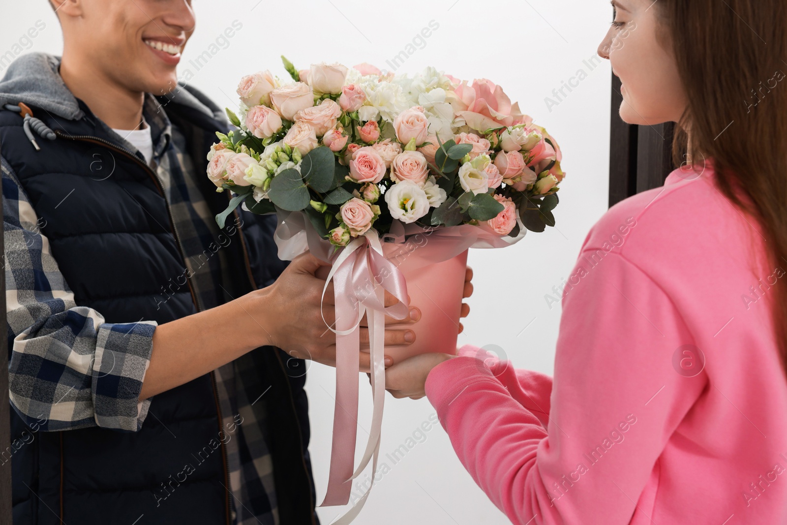 Photo of Happy delivery man giving gift box with beautiful floral composition to woman on white background, closeup