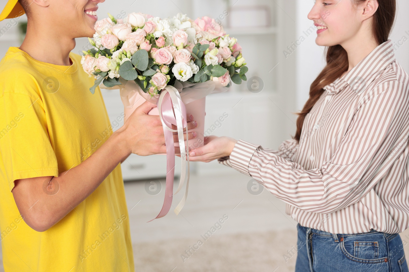 Photo of Happy delivery man giving gift box with beautiful floral composition to woman indoors, closeup