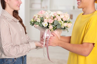 Delivery man giving gift box with beautiful floral composition to woman indoors, closeup