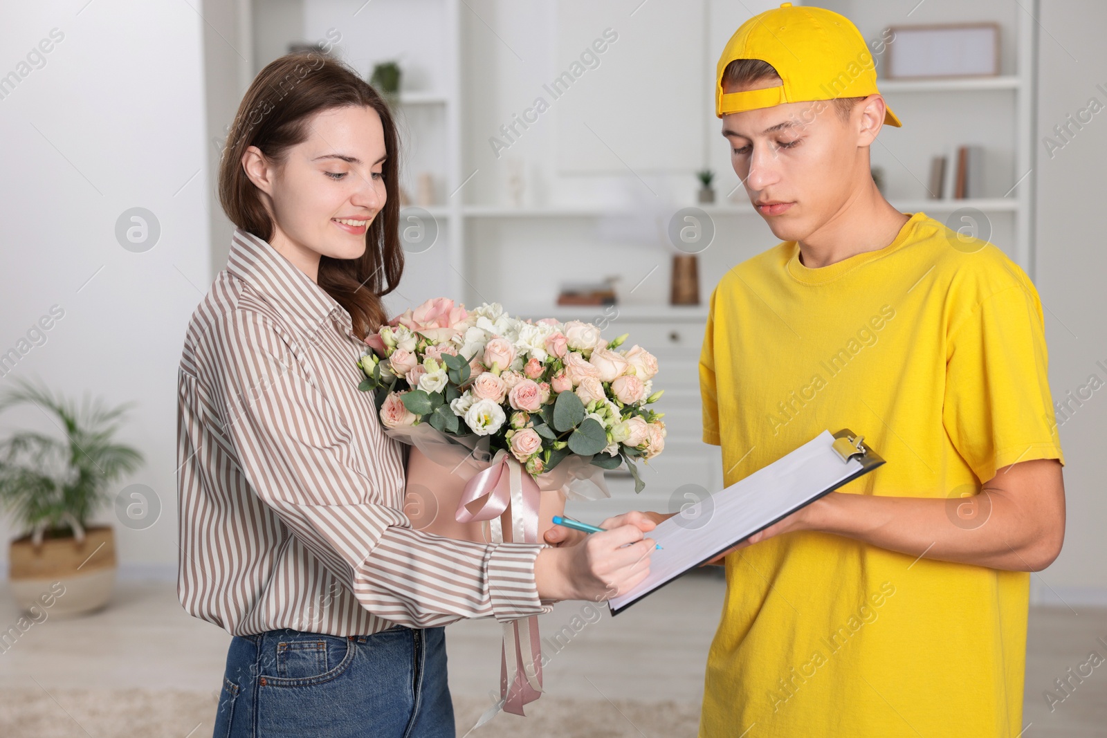 Photo of Smiling woman signing for delivered gift box with floral composition indoors