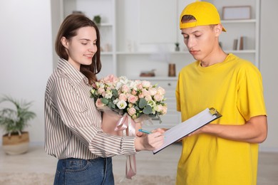 Smiling woman signing for delivered gift box with floral composition indoors