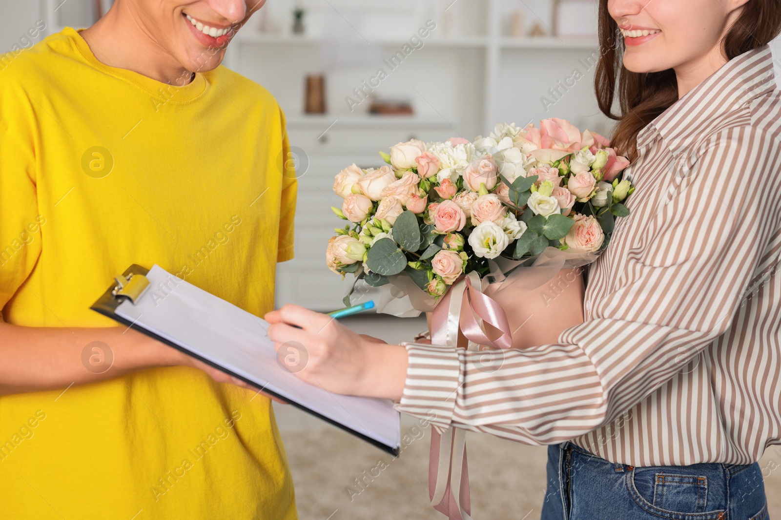 Photo of Smiling woman signing for delivered gift box with floral composition indoors, closeup