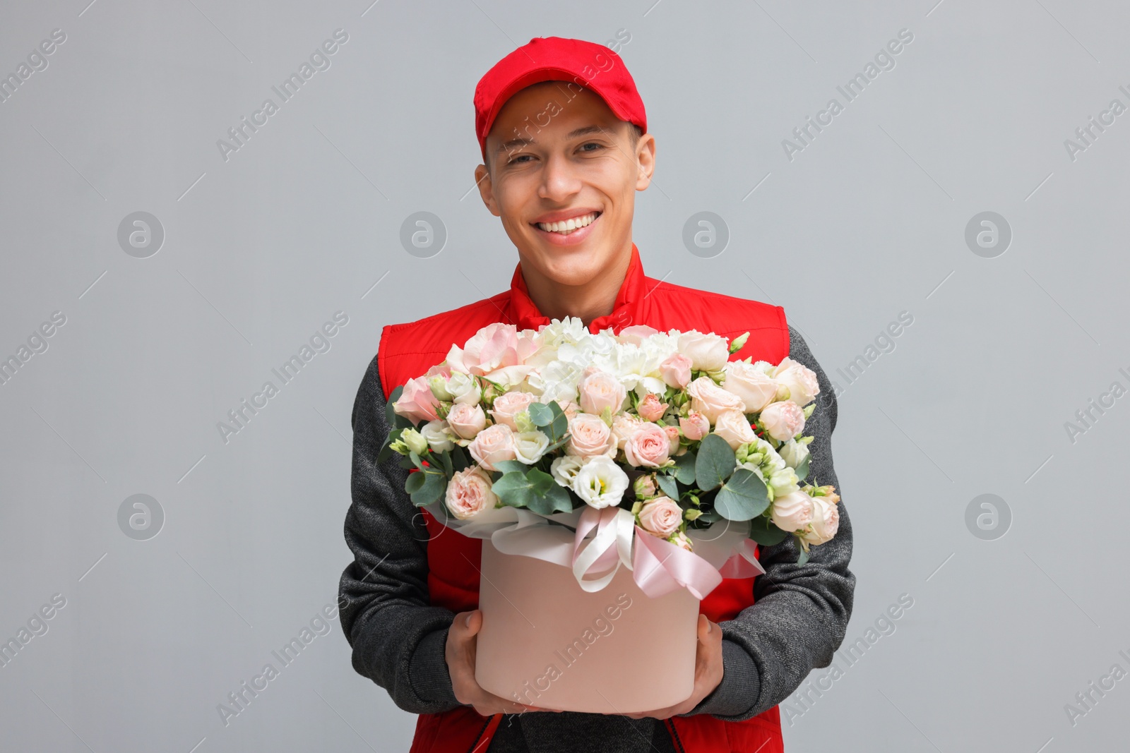 Photo of Smiling delivery man holding gift box with beautiful floral composition on grey background