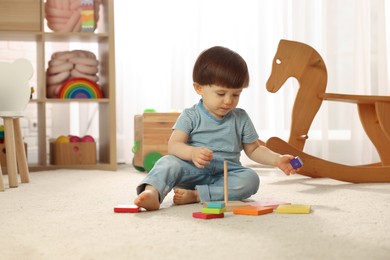 Photo of Cute little boy playing with toy pyramid on floor at home