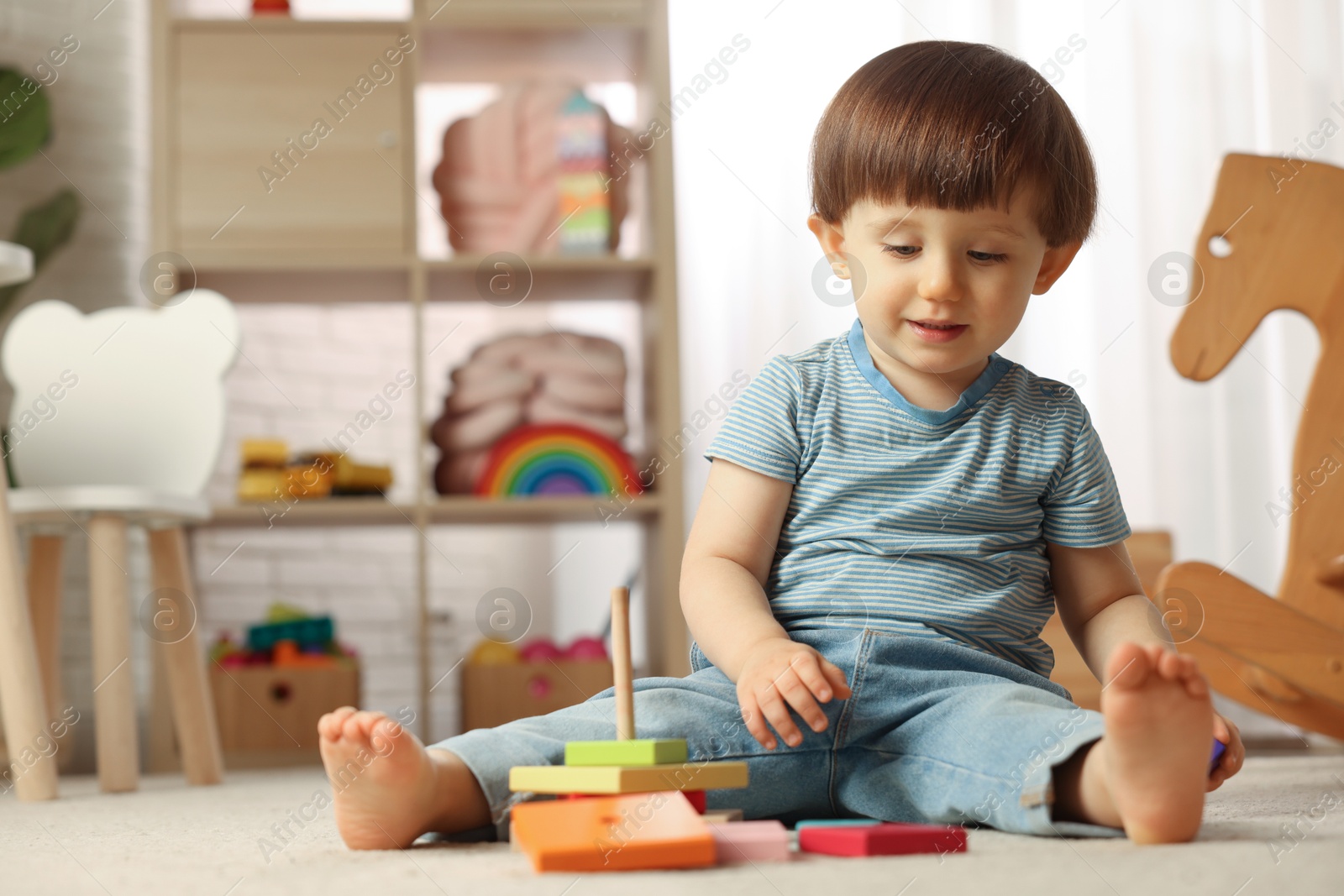 Photo of Cute little boy playing with toy pyramid on floor at home, space for text