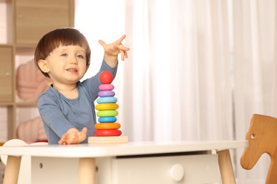 Photo of Cute little boy playing with toy pyramid at table indoors, space for text