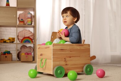 Photo of Cute little boy playing in wooden cart at home