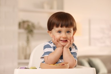 Photo of Cute little boy sitting in high chair at home