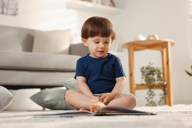 Photo of Cute little boy with book on floor at home