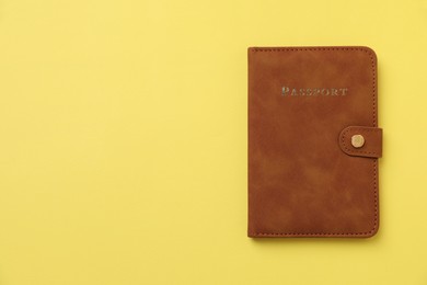 Photo of Passport in leather cover on yellow background, top view. Space for text