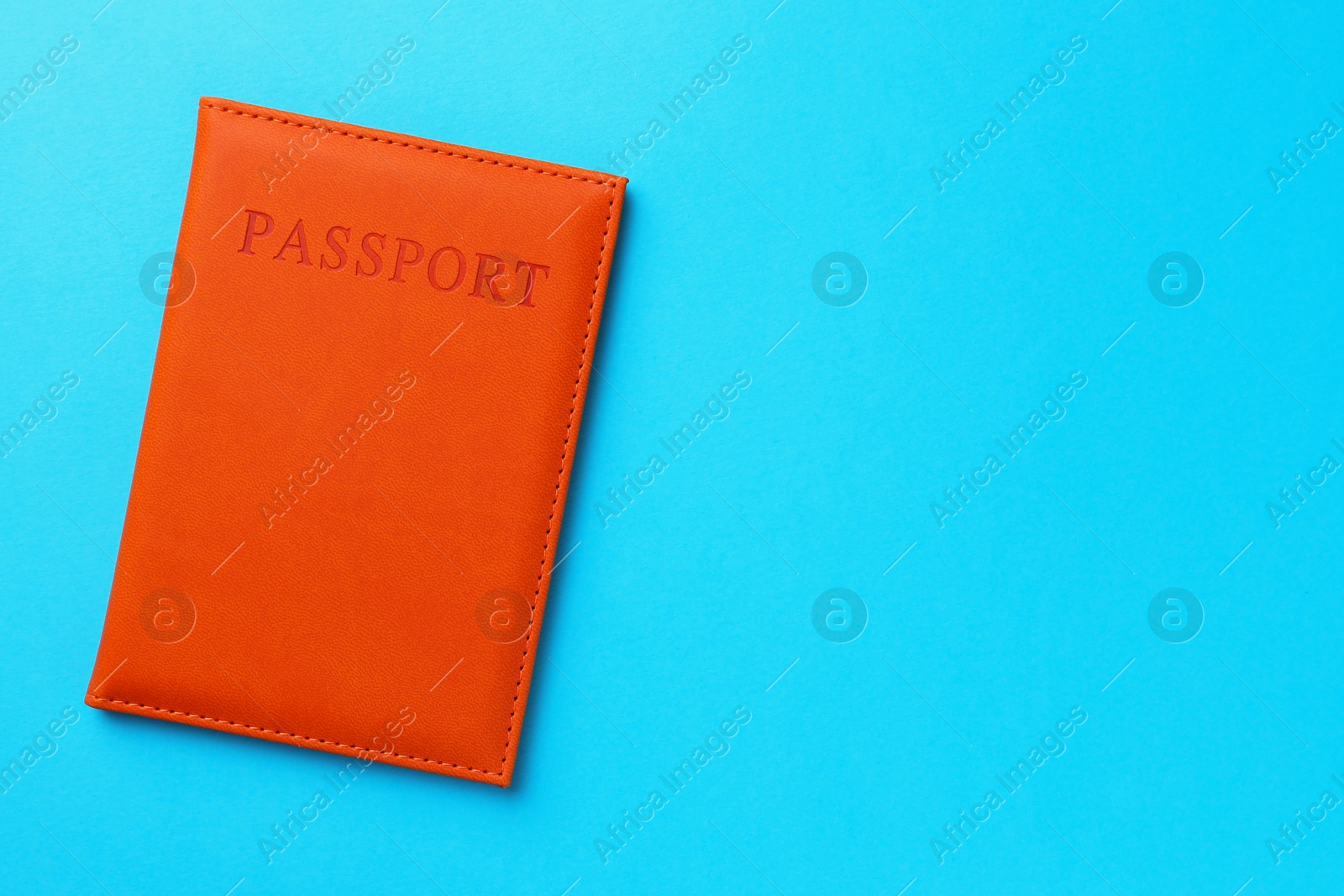 Photo of Passport in orange cover on light blue background, top view. Space for text