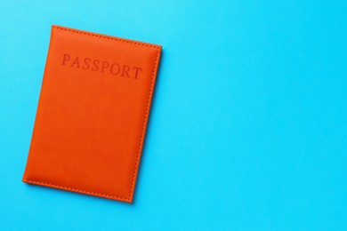 Photo of Passport in orange cover on light blue background, top view. Space for text