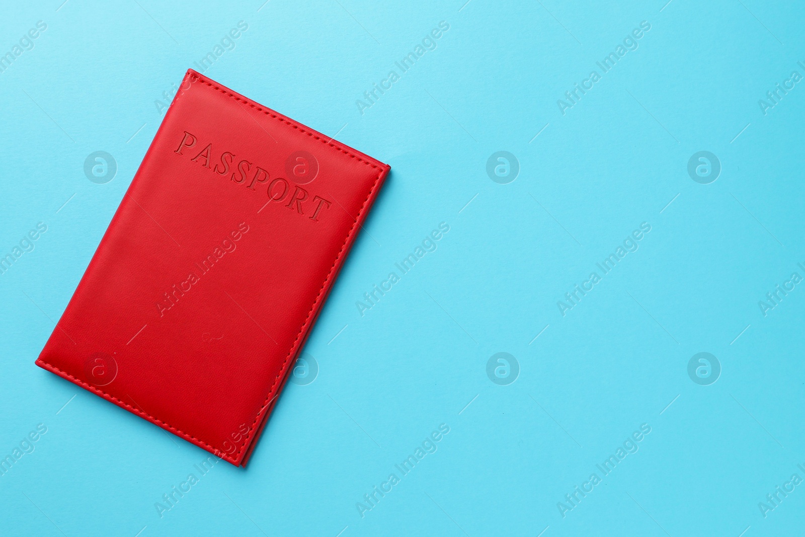 Photo of Passport in red cover on light blue background, top view. Space for text