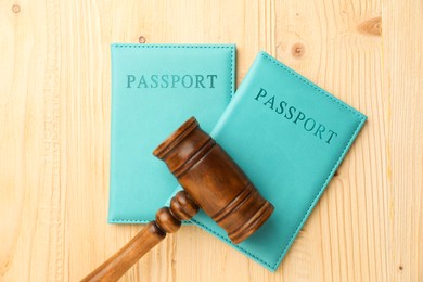 Photo of Passports in light blue covers and judge's gavel on wooden table, top view