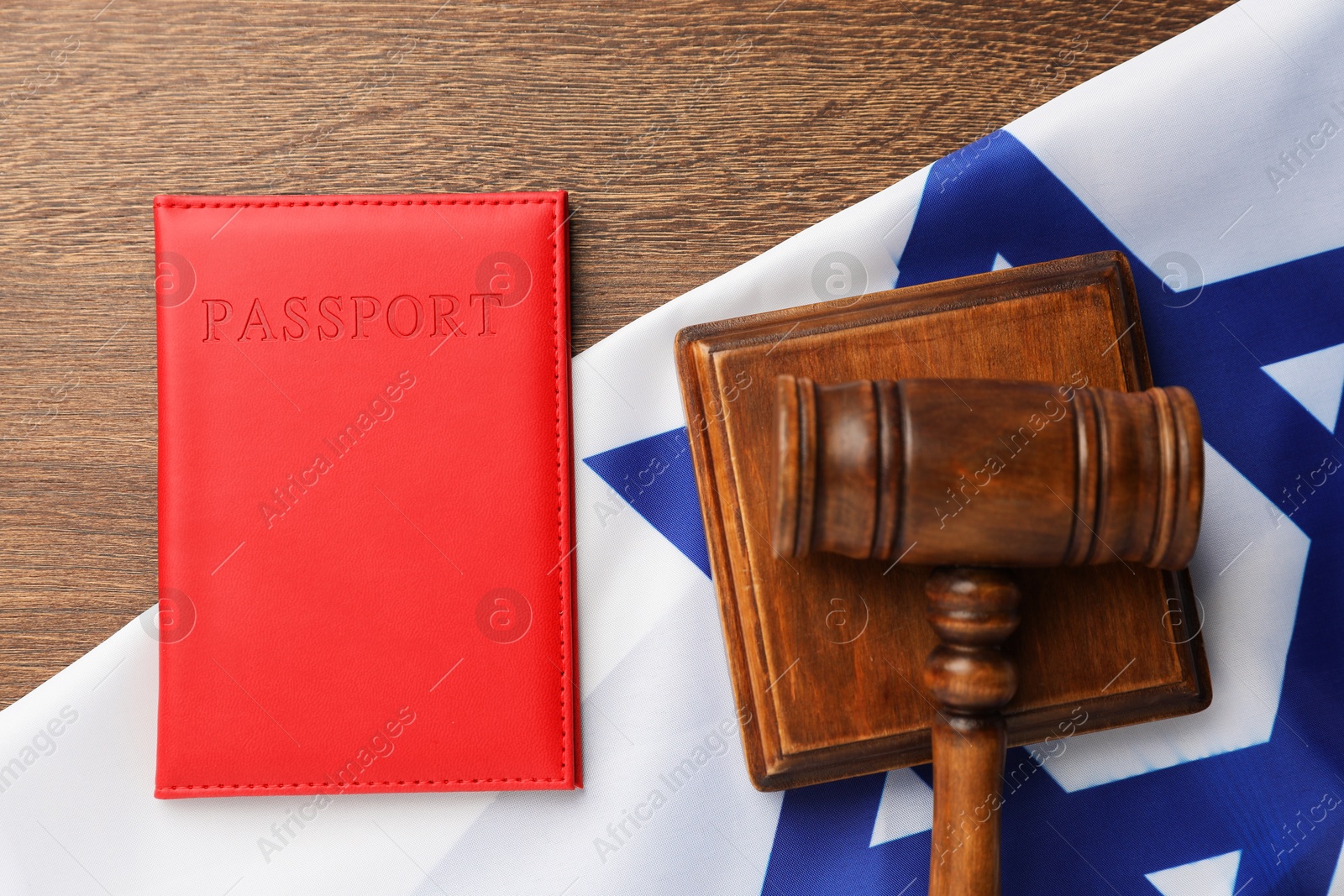 Photo of Passport in red cover, gavel and flag of Israel on wooden table, top view