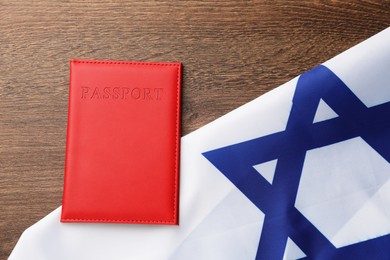 Photo of Passport in red cover and flag of Israel on wooden table, top view