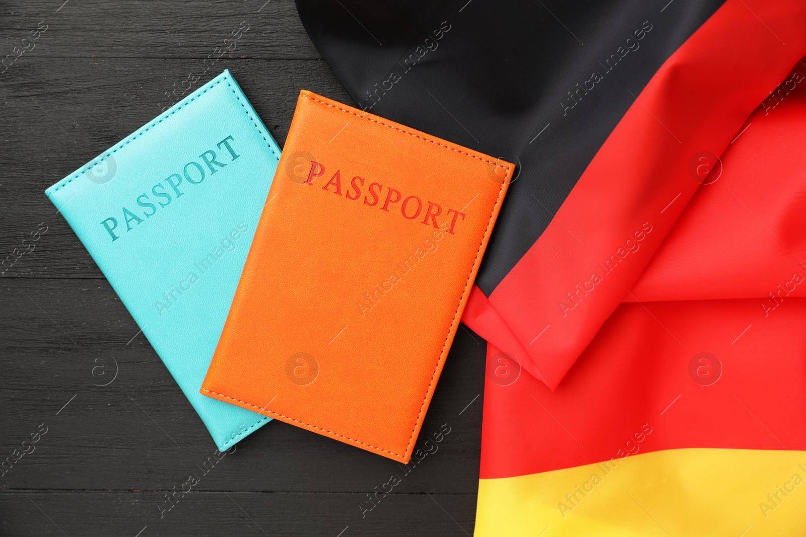 Photo of Passports in color covers and flag of Germany on black wooden table, top view