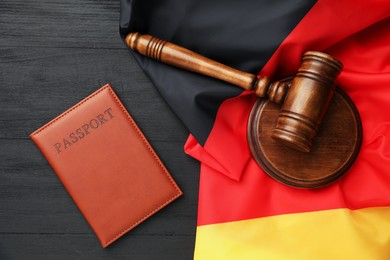 Photo of Passport in brown cover, gavel and flag of Germany on black wooden table, top view