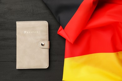 Photo of Passport in leather cover and flag of Germany on black wooden table, top view