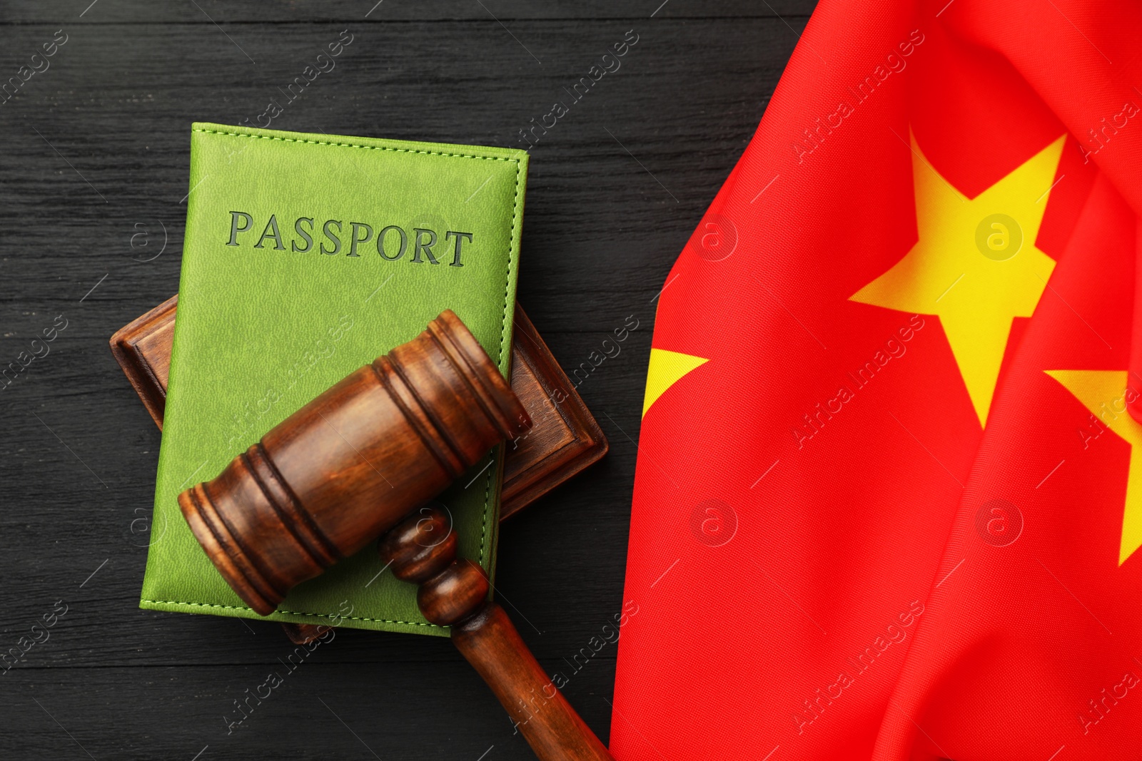 Photo of Passport in green cover, gavel and flag of China on black wooden table, top view