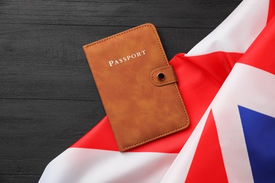 Photo of Passport in brown cover and flag of United Kingdom on black wooden table, top view