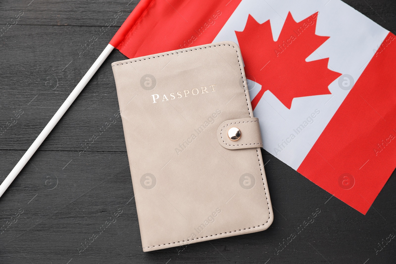 Photo of Passport in leather cover and flag of Canada on black wooden table, top view