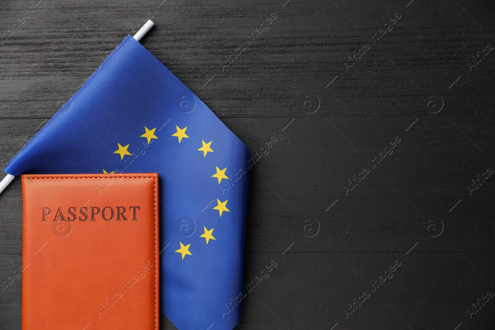 Photo of Passport in brown cover and flag of European Union on black wooden table, top view. Space for text