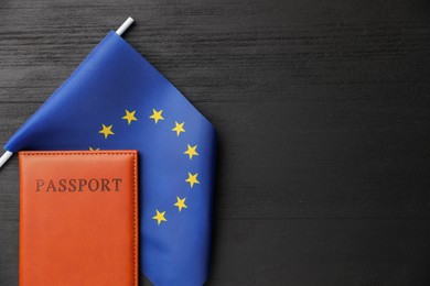 Photo of Passport in brown cover and flag of European Union on black wooden table, top view. Space for text