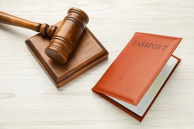 Photo of Passport in brown cover and judge's gavel on light wooden table, above view