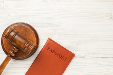 Photo of Passport in brown cover and judge's gavel on light wooden table, top view. Space for text