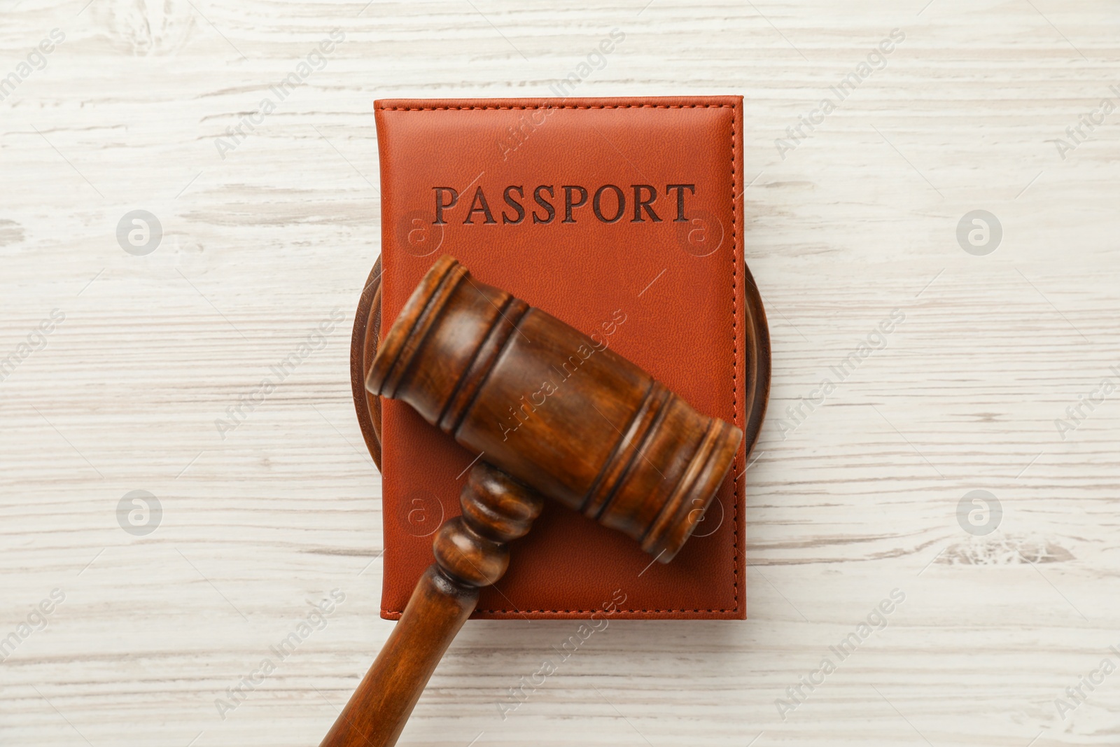 Photo of Passport in brown cover and judge's gavel on light wooden table, top view