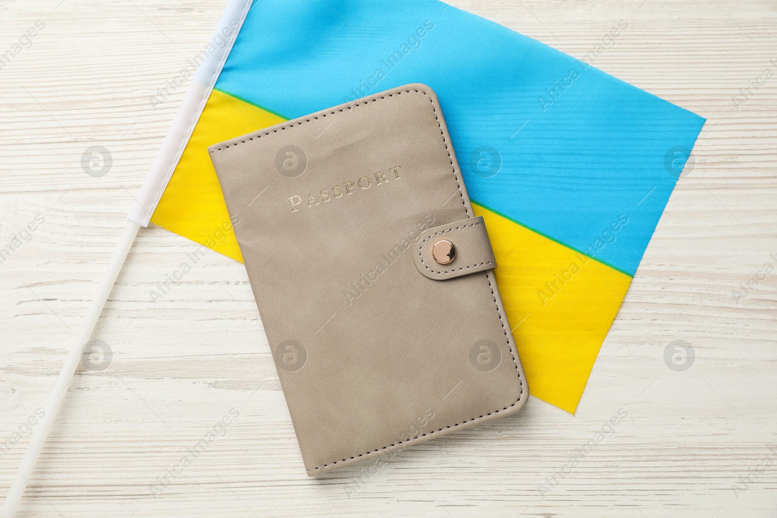 Photo of Passport in leather cover and flag of Ukraine on light wooden table, top view