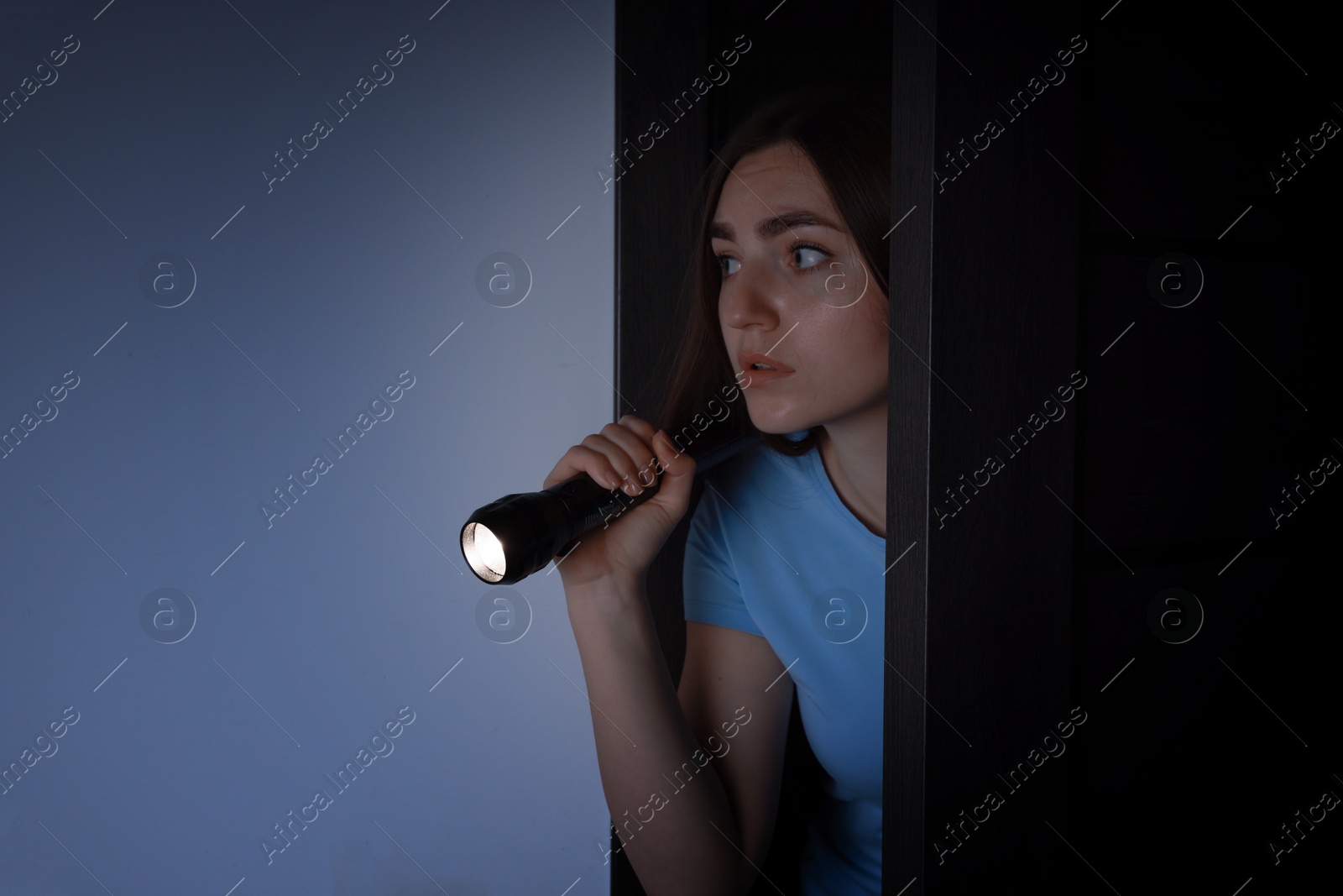 Photo of Fear of darkness. Scared young woman with flashlight indoors at night