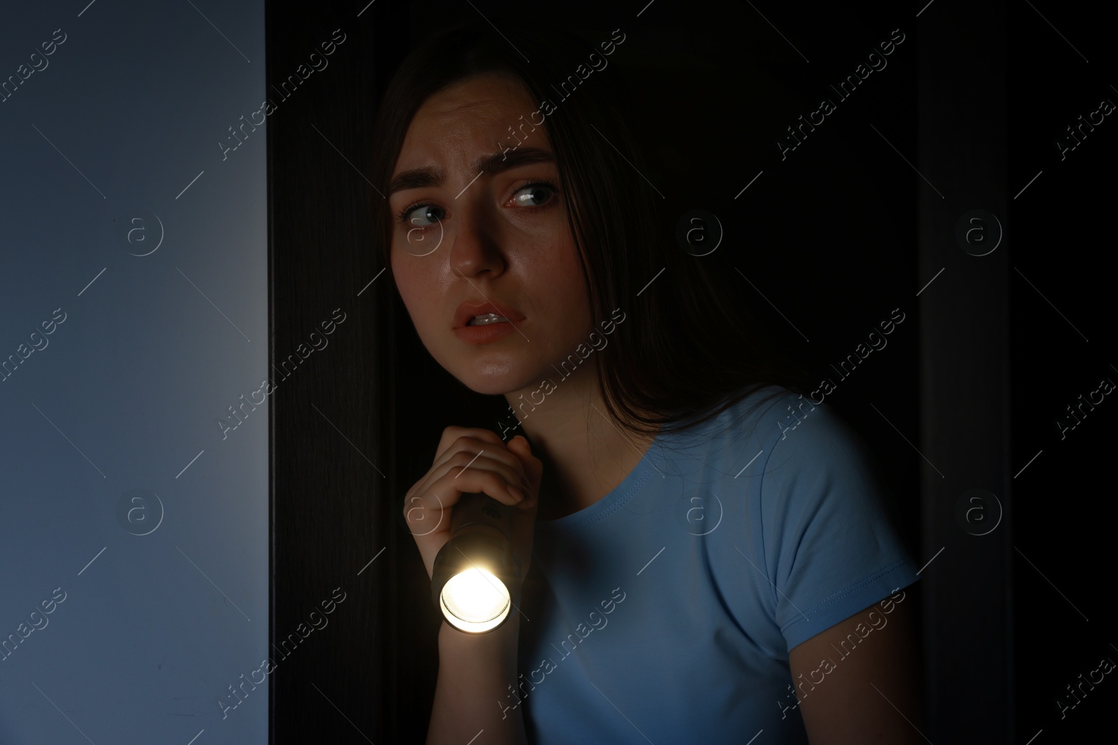 Photo of Fear of darkness. Scared young woman with flashlight indoors at night