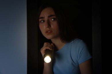 Photo of Fear of darkness. Scared young woman with flashlight indoors at night