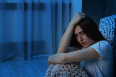 Photo of Fear of darkness. Scared young woman with blanket near couch indoors at night, space for text