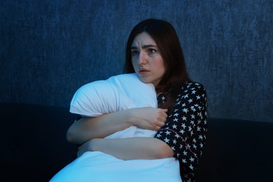 Photo of Fear of darkness. Scared young woman hugging pillow on couch indoors at night