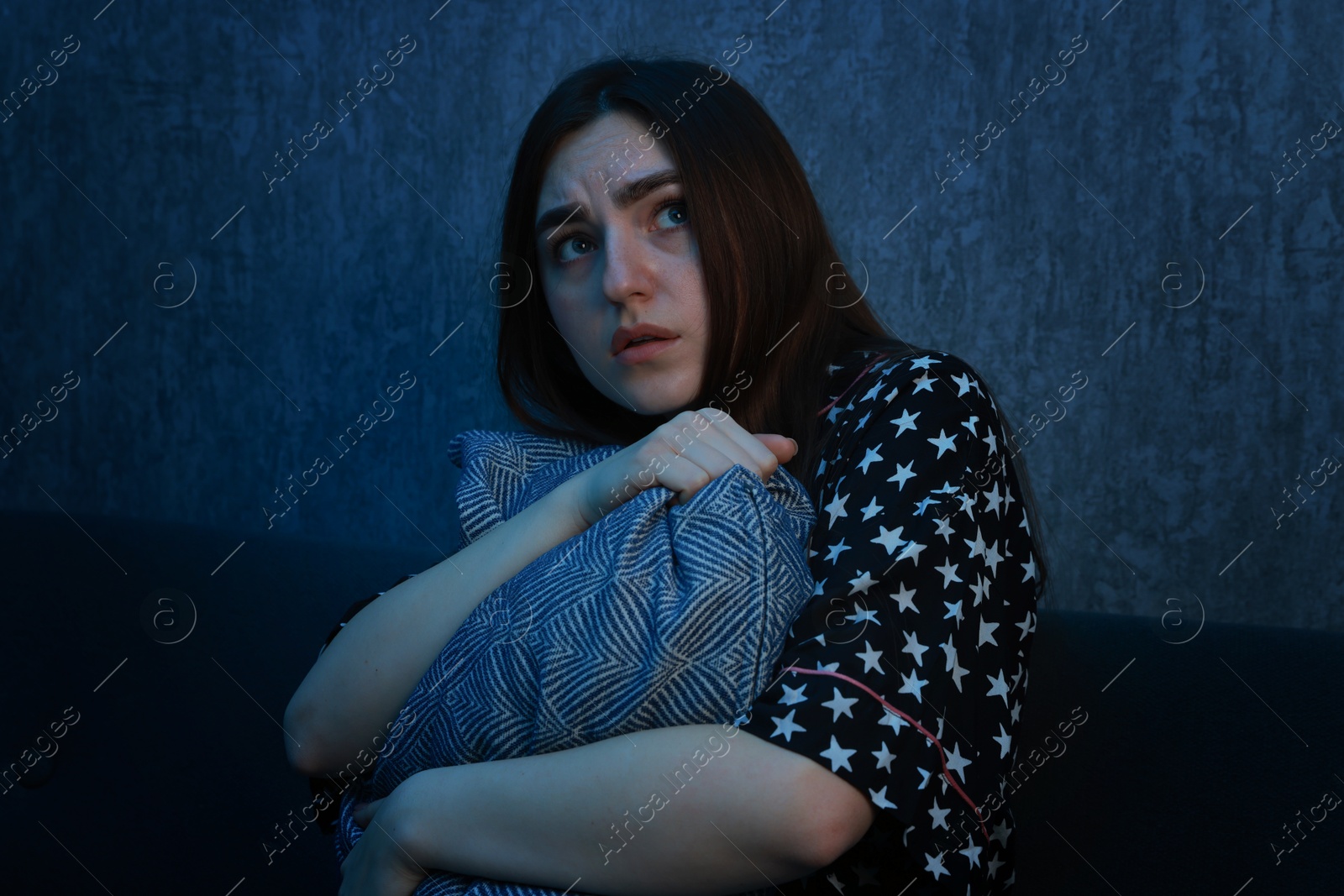 Photo of Fear of darkness. Scared young woman hugging pillow on couch indoors at night