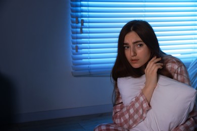 Photo of Fear of darkness. Scared young woman hugging pillow in bedroom at night, space for text