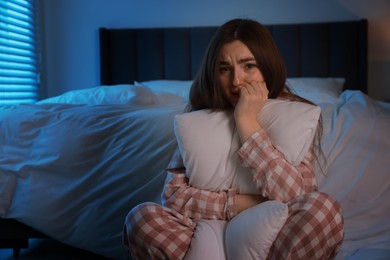 Photo of Fear of darkness. Scared young woman hugging pillow in bedroom at night