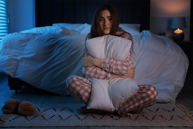 Photo of Fear of darkness. Scared young woman hugging pillow in bedroom at night