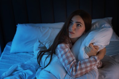 Photo of Fear of darkness. Scared young woman lying on bed in room at night, space for text