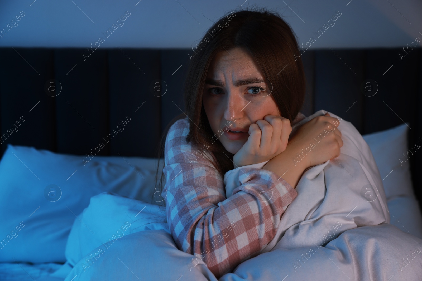 Photo of Fear of darkness. Scared young woman lying on bed in room at night