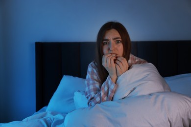 Photo of Fear of darkness. Scared young woman lying on bed in room at night, space for text