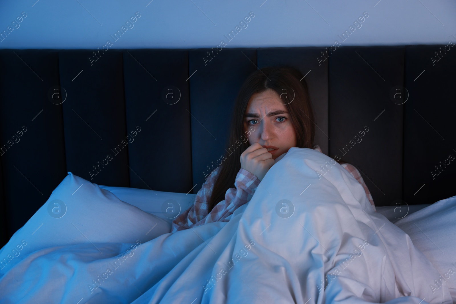 Photo of Fear of darkness. Scared young woman lying on bed in room at night, space for text