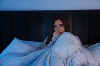 Photo of Fear of darkness. Scared young woman lying on bed in room at night, space for text