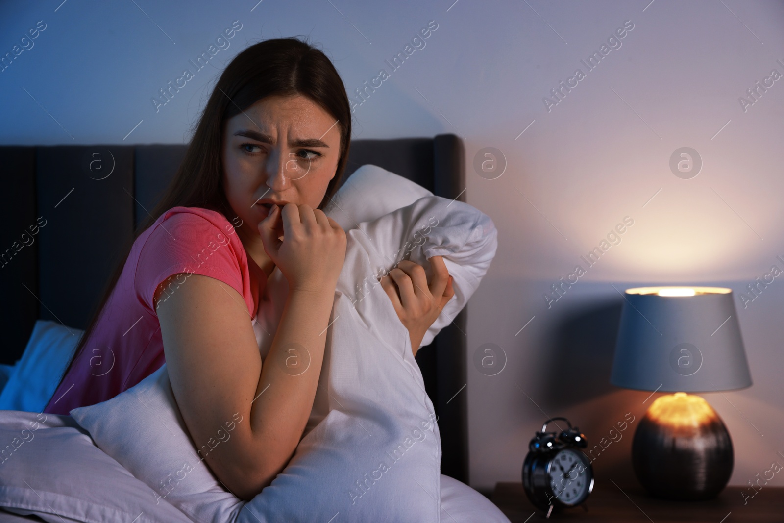 Photo of Fear of darkness. Scared young woman on bed in room at night, space for text