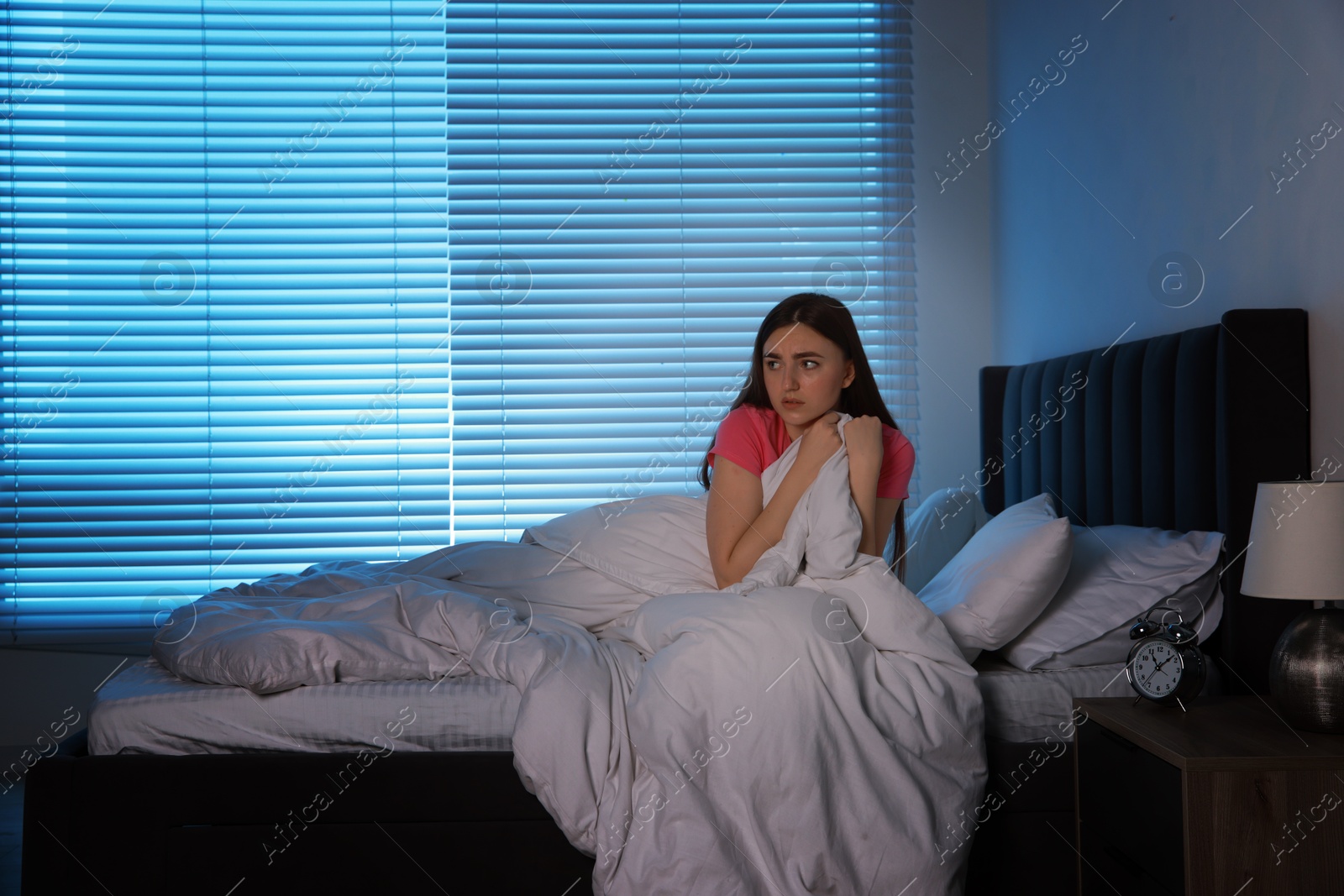 Photo of Fear of darkness. Scared young woman on bed in room at night, space for text