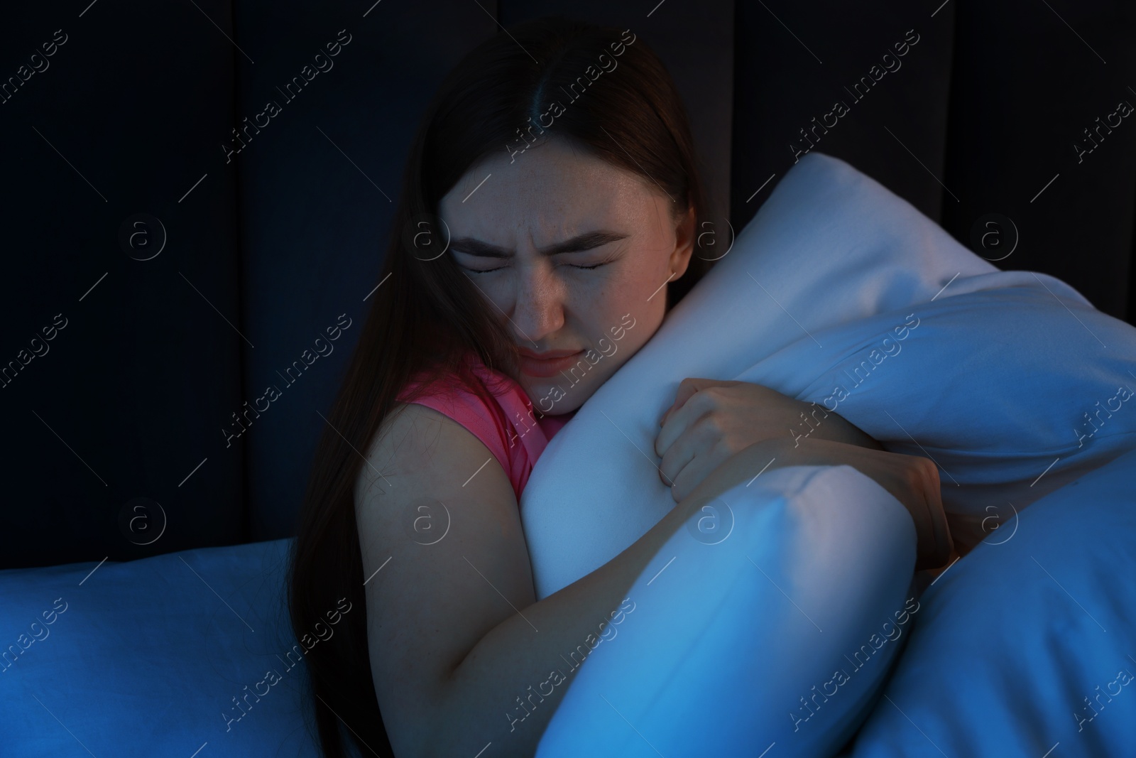 Photo of Fear of darkness. Scared young woman on bed in room at night